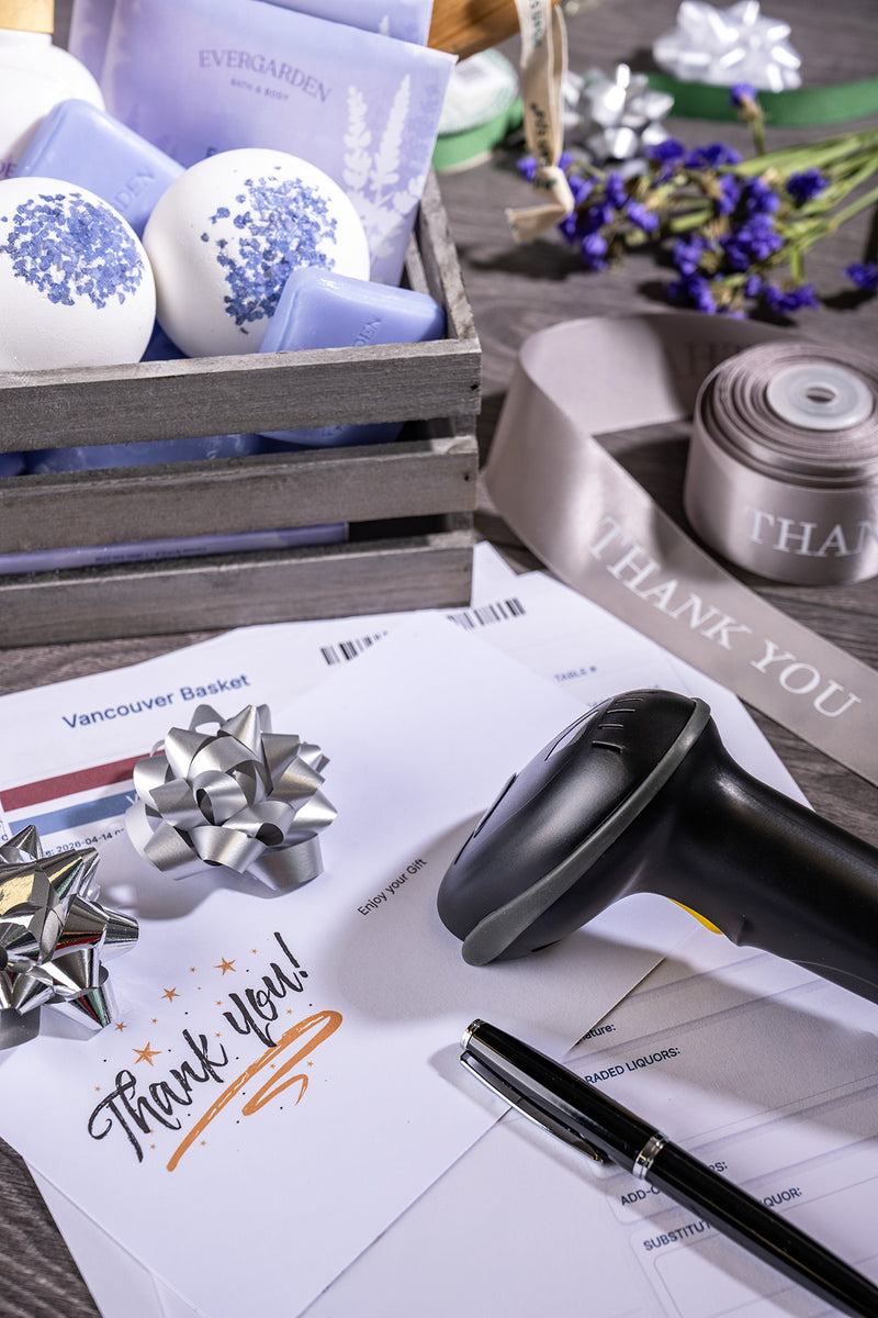 Elegant thank-you gift flat lay with floral cards, white candles, ribbon bows, black pen, and sleek reader device on a soft gray table.
