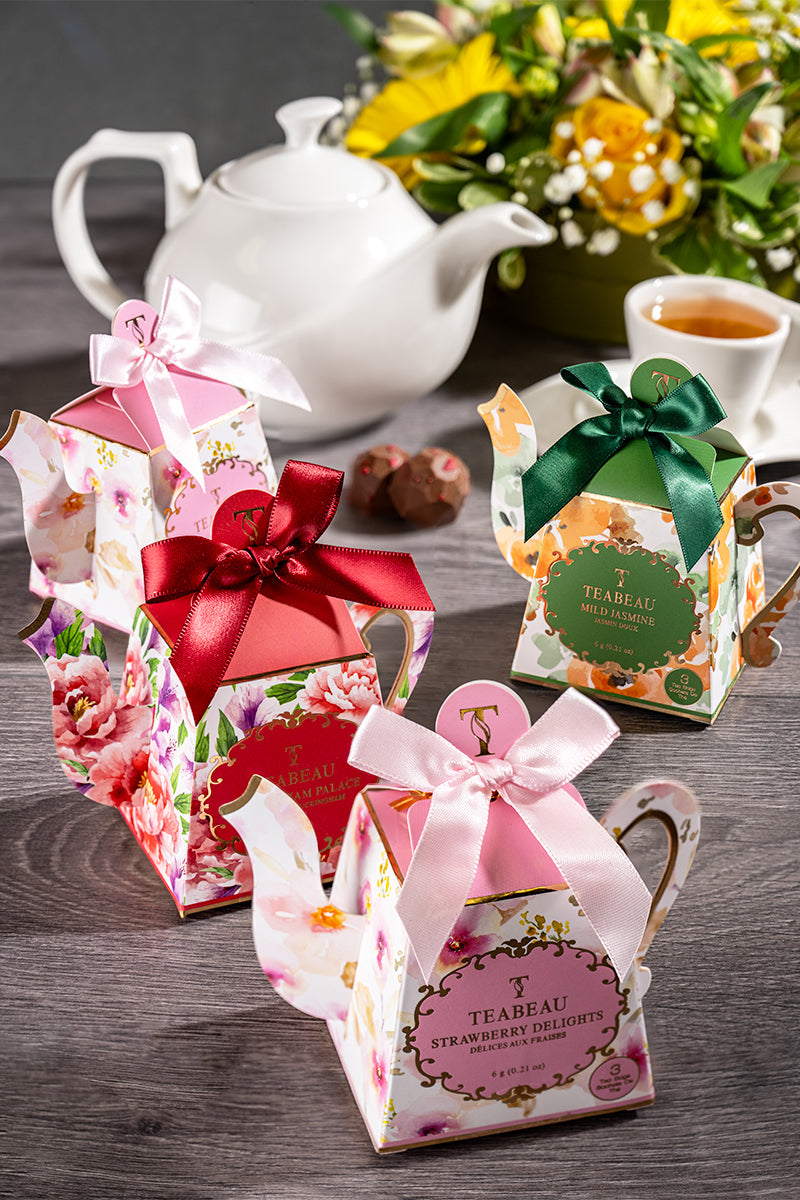 Elegant tea gift boxes with satin bows beside a white teapot, cup, flowers, and chocolates on a dark table, festive and refined.
